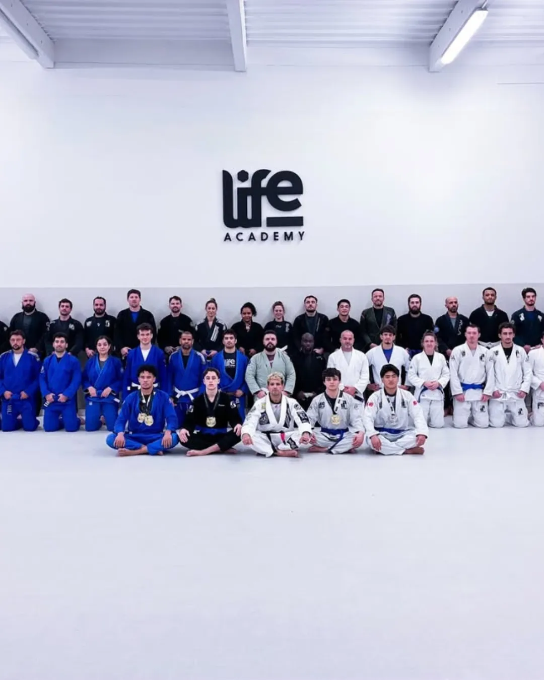 Photo de groupe des adhérents en kimono sur le tatami, sous le logo Life Academy