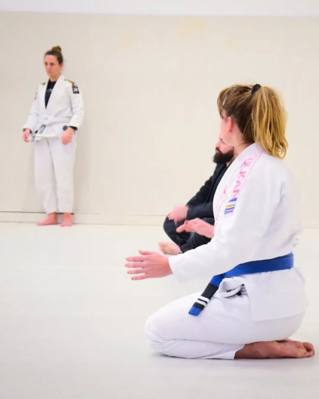 Cours adultes : deux pratiquantes en kimono blanc, l’une à genoux, écoutent la consigne